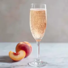 Ett glas bubblig Bellini drink med persika bredvid.