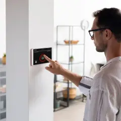Hombre interactúa con pantalla táctil de domótica, controlando luces y seguridad. Los sensores domotica hacen el hogar inteligente.