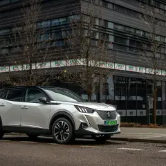 Biały Peugeot e-2008 zaparkowany przed nowoczesnym budynkiem.
