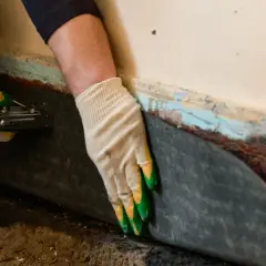 Hände mit Handschuhen befestigen eine schwarze Folie an einer Wand. Dies ist eine vertikalsperre von innen, um Feuchtigkeit fernzuhalten.