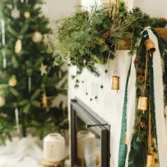 Urocza girlanda DIY z gałązek sosny, szyszek i złotych dzwoneczków ozdabia kominek. W tle choinka.