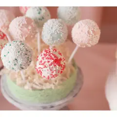 Bunte Kuchen am Stiel, verziert mit Perlen und Streuseln, auf einem grünen Podest arrangiert.