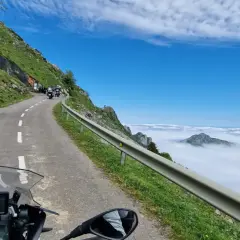 Motociclistas en un viaje por carretera, con un paisaje montañoso y nubes. El significado de este trip km es la aventura.