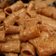 En närbild på rigatoni pasta i en krämig ost och skinksås. Pastan är täckt av såsen som ser smakrik ut.