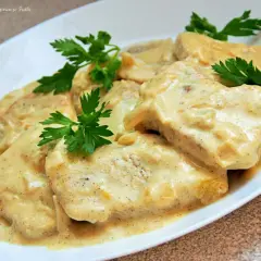 Pyszny filet z indyka w sosie śmietanowym, udekorowany natką pietruszki. Danie wygląda apetycznie i zachęca do spróbowania.