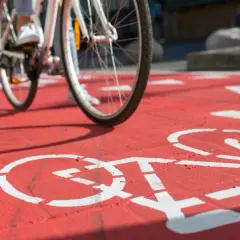 Rowerzysta nabiera prędkości na czerwonej ścieżce rowerowej, gdzie białe symbole rowerów wyznaczają trasę.
