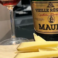 Verre de vin et fromage sur planche en bois, à côté d'une bouteille de Maury. La question est : que boire avec du fromage ?