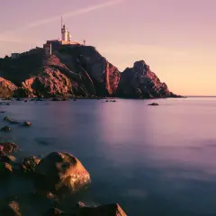 Faro en Cabo de Gata al atardecer, con rocas en primer plano y el mar en calma. Un lugar perfecto para disfrutar de la tranquilidad, como en el bar La Estrella.