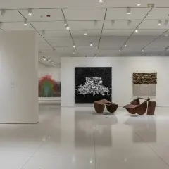 An art gallery features diverse works, including a colorful draped sculpture, a black and white textured piece, and a vibrant collage, reminiscent of the bold style of Pamela Joyner.