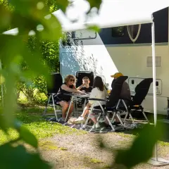 Family playing cards at a table outside a camper van on a sunny day.