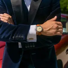 Elegancki mężczyzna w granatowym aksamitnym garniturze i białej koszuli pokazuje, jak nosić zegarek do koszuli. Klasyczny styl.