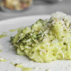 Kremowe risotto ze szparagami, posypane parmezanem i migdałami, na białym talerzu.