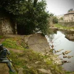 Escultura de hombre pensativo junto a un río, con una casa de piedra reflejada en el agua. Un lugar tranquilo que ver cerca de Liérganes.