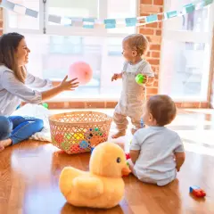 Mama bawi się z dziećmi, rzucając różową piłeczką. Wesołe gry logopedyczne dla 4 latka, pełne kolorowych zabawek w koszyku.