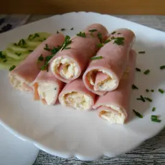 Roladki z twarogiem, zawinięte w plastry szynki, ozdobione szczypiorkiem i podane z plasterkami ogórka.