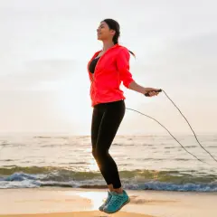 Uśmiechnięta kobieta skacze na skakance na plaży o wschodzie słońca. Widać pierwsze efekty po 2 tygodniach treningów.