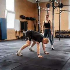 Mężczyzna wykonuje burpee pod okiem trenerki w siłowni.