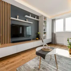 Nowoczesna ozdobna ściana w salonie z drewnianymi lamelami, telewizorem i białymi szafkami.