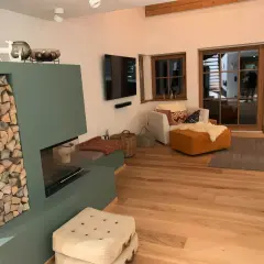 Gemütliches Wohnzimmer im modernen Landhausstil mit Kamin, Holzfußboden und großen Glasfronten.