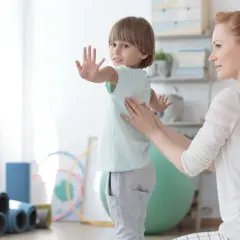 Ein Kind mit Skoliose erhält osteopathische Behandlung. Eine Therapeutin legt sanft die Hände auf den Rücken des Jungen, der sich leicht wegdreht.