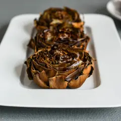 Tres alcachofas al horno, doradas y crujientes, listas para disfrutar. El tiempo perfecto de cocción resalta su sabor.