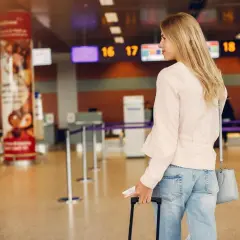 Odprawa na lotnisku w Katowicach: młoda kobieta z walizką i dokumentami czeka przy stanowisku odprawy, widoczne tablice z numerami lotów.
