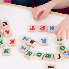 Dzieci układają litery na tablicy, ćwicząc podział na głoski. Widoczne litery to m.in. U, A, T, R, E, N, K, P, Z, O, B, J, I.
