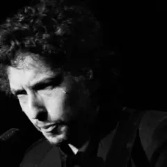 Bob Dylan, ikoniskt ansikte i en svartvit film, med lockigt hår och intensiv blick.