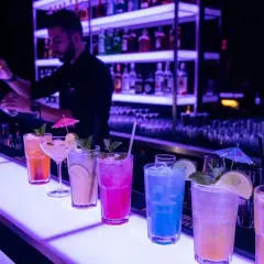 Kolorowe drinki na barze, barman przygotowuje kolejny. Idealne miejsce na relaks i smakowanie wyśmienitego **alkoholu** na **Malcie**.