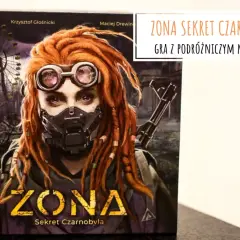 ZONA: Sekret Czarnobyla – gra planszowa z podróżniczym motywem. Postać z rudymi dredami, goglami i maską ochronną, na tle zrujnowanego diabelskiego młyna.
