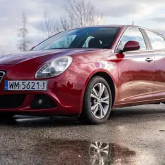 Czerwone Alfa Romeo Giulietta na mokrej drodze. Wiele osób szuka alfa romeo giulietta opinie przed zakupem.