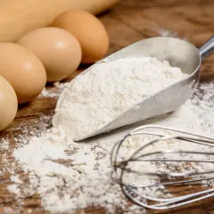 Jajka, mąka w szufelce, wałek i trzepaczka na drewnianym blacie.
