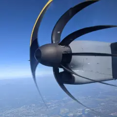 Wirujący silnik samolotu z widocznym efektem rolling shutter. W tle błękitne niebo i krajobraz z lotu ptaka.