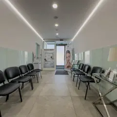 Nowoczesna poczekalnia z czarnymi krzesłami, podświetlanym sufitem i banerem reklamowym.