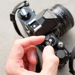 A hand adjusts the ISO dial on a vintage film camera, showing its mechanical controls.