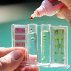 Teststreifen misst pH & Chlor im Pool. Tropfen einer roten Flüssigkeit fallen hinein. Hausmittel zur Chlor-Senkung sind hier nicht zu sehen.