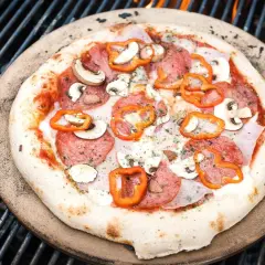 Eine köstliche Pizza mit Salami, Pilzen und Paprika wird auf einem Pizzastein über glühenden Kohlen auf dem Grill zubereitet.