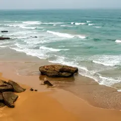 Maroko morze. Dwie osoby z deskami surfingowymi wchodzą do wody na piaszczystej plaży, fale rozbijają się o skaliste wybrzeże.