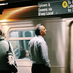 Personas esperando un tren en el metro de Nueva York con un letrero de destino.