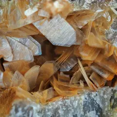 Nahaufnahme von Anhydrit-Kristallen, die wie dünne, schichtartige Plättchen in warmen Orangetönen und transparenten Farben angeordnet sind.