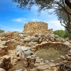 Rovine di un nuraghe in pietra sotto un cielo azzurro. Un mistero su chi ha costruito i nuraghi.