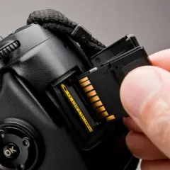 Dłoń wkłada kartę pamięci do aparatu. Różne rodzaje kart pamięci, takie jak SD, microSD, CompactFlash, są kluczowe dla przechowywania danych.