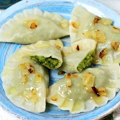 Pyszne pierogi z bobem, polane skwarkami z cebulki, na niebieskim talerzu.