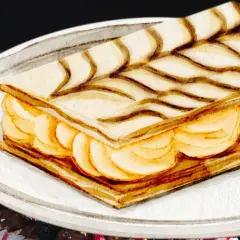 Gâteau rectangulaire avec des couches de pâte feuilletée et de crème pâtissière, décoré de fines lignes chocolatées.