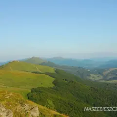 Widok na zielone, falujące wzgórza Bieszczadów z krętymi ścieżkami i lasami w tle.
