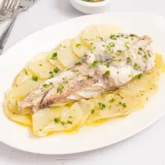 Rape al horno servido sobre patatas laminadas y espolvoreado con perejil fresco.