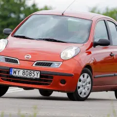 Pomarańczowy Nissan Micra K12 na drodze, z zielenią w tle.
