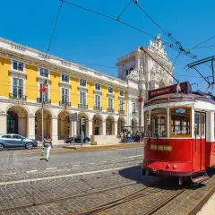 Czerwony tramwaj w Lizbonie, obok żółtego budynku z arkadami. Czy do Portugalii potrzebny jest paszport? Tak, jeśli nie jesteś obywatelem UE.