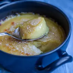En sked lyfter en bit av krämig, karamelliserad vegansk creme brulee ur en mörkblå skål.