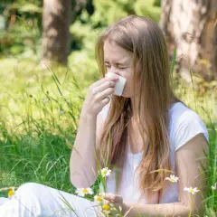 Dziewczyna w trawie z chusteczką przy nosie, cierpiąca na co na alergie na trawy.